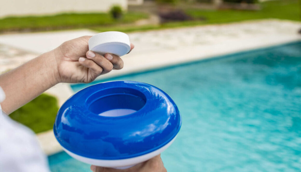 Hands holding a dispenser with pool chlorine tablet, pool float and chlorine tablets for pool maintenance. Hands holding a pool chlorine dispenser. Hand of a pool disinfection worker holding a dispenser with a chlorine tablet.