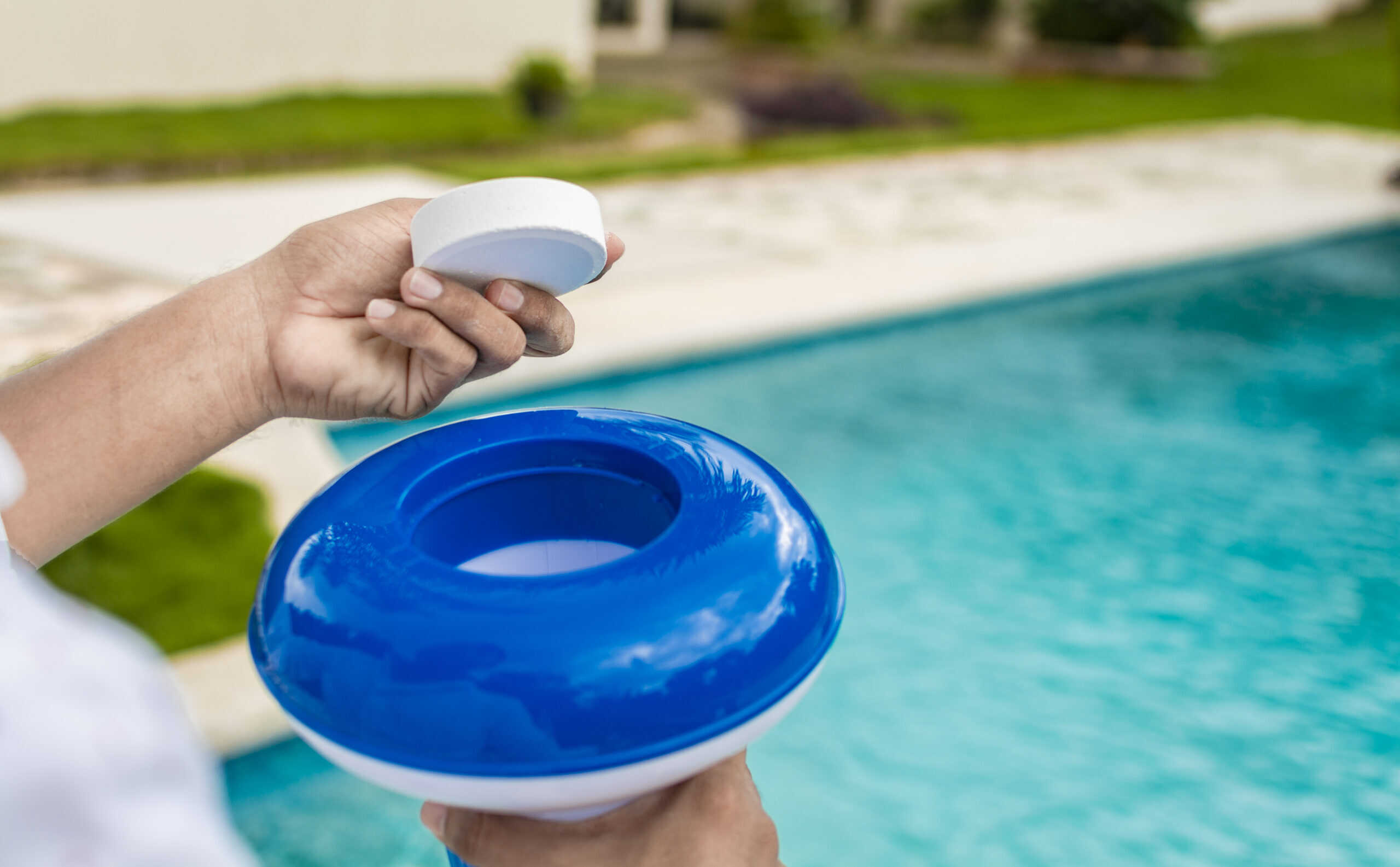 Hands holding a dispenser with pool chlorine tablet, pool float and chlorine tablets for pool maintenance. Hands holding a pool chlorine dispenser. Hand of a pool disinfection worker holding a dispenser with a chlorine tablet.