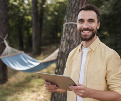 smiley-man-holding-tablet-while-camping-outdoors
