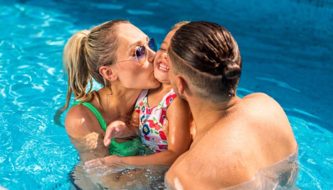 happy-parents-kissing-their-smiling-daughter-while-swimming-pool_0x800
