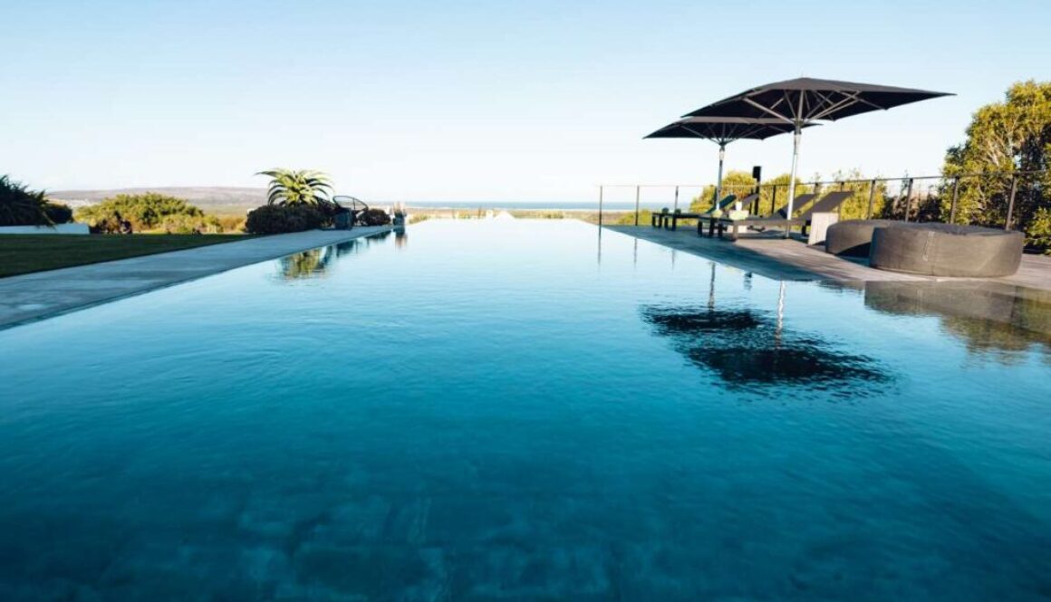 empty-deckchairs-umbrella-arranged-by-swimming-pool-against-clear-blue-sky-nursing-home-copy-space-water-reflection-unaltered-support-assisted-living-retirement-home_0x800